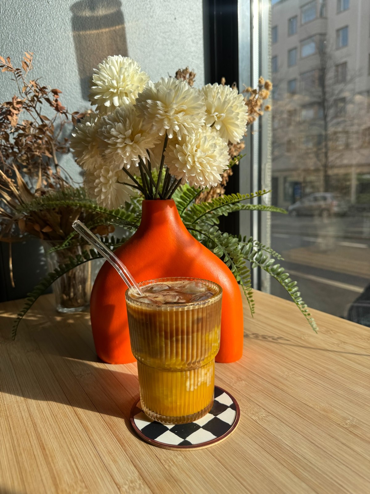 An iced golden drink on the café windowsill beside orange flowers