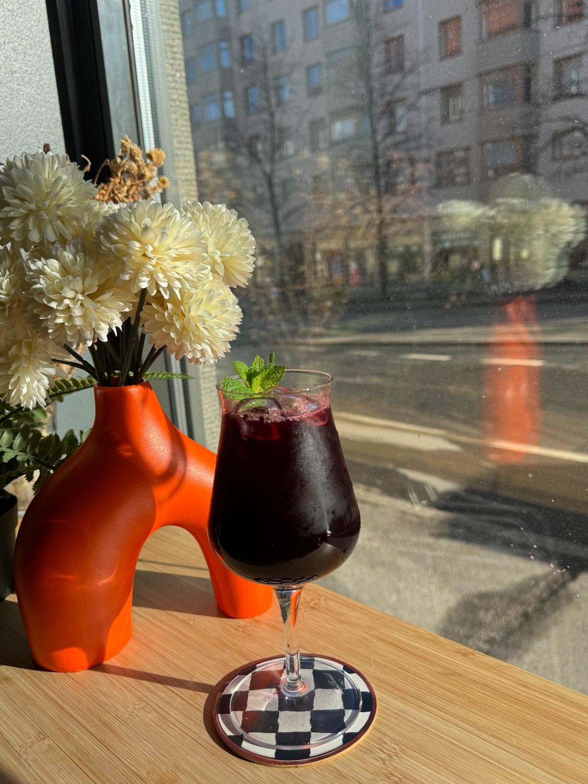 A dark red iced drink garnished with lime by the café window