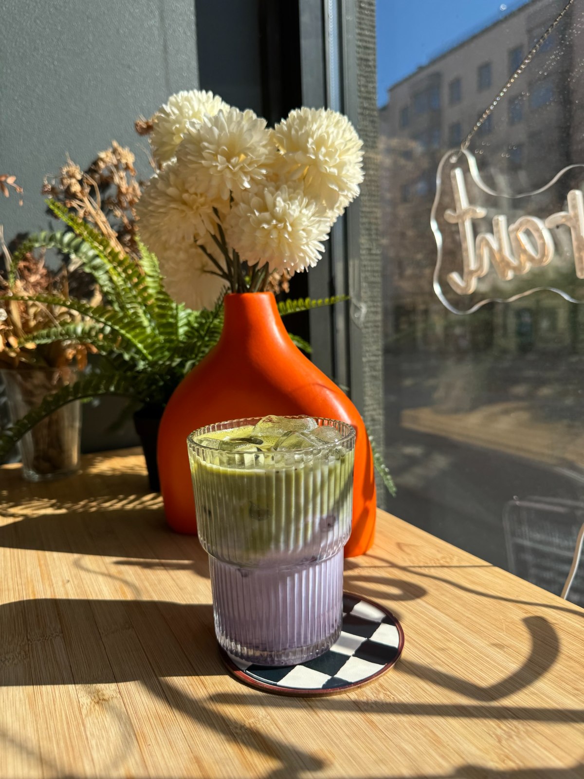 A colourful layered drink beside flowers in the café window